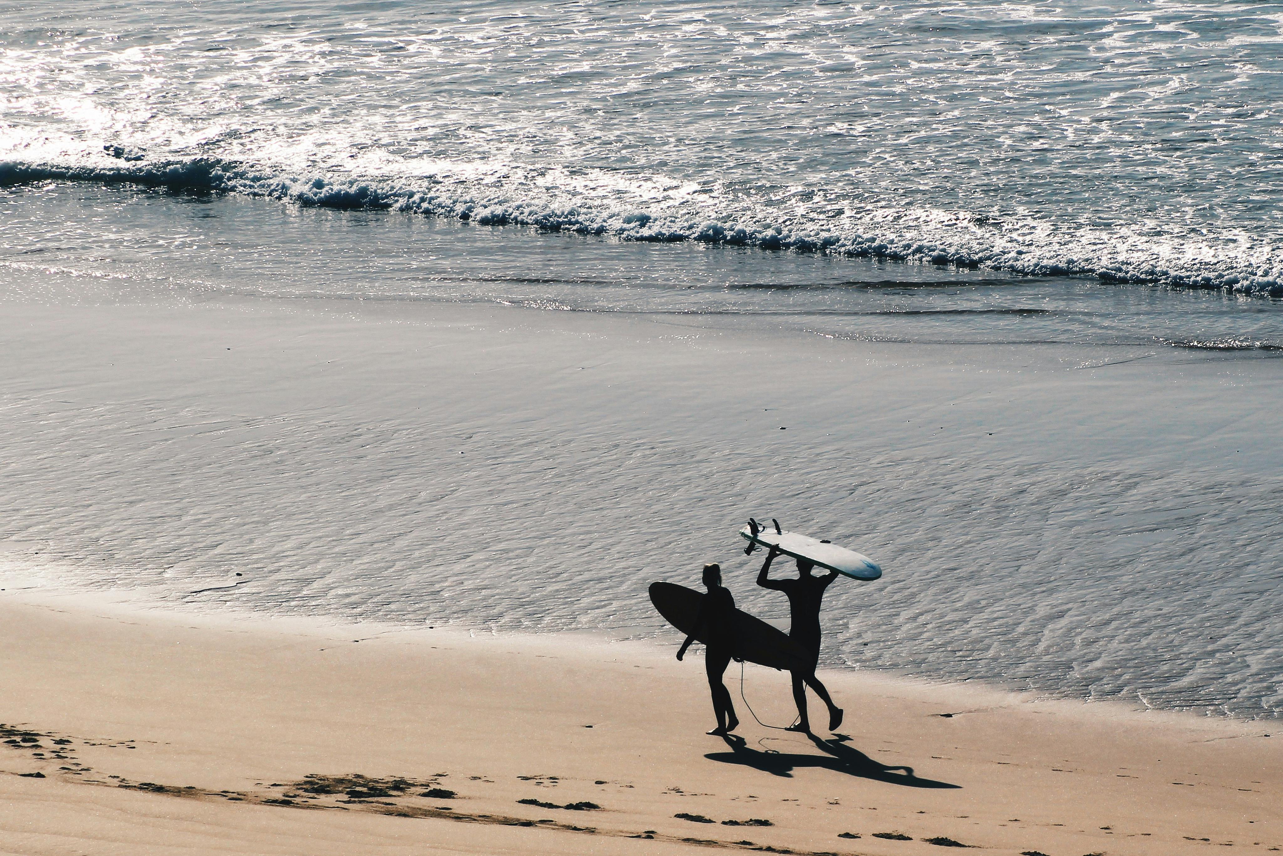 Two surfers carrying boards on Sagres beach, Portugal, evoke the essence of summer adventure.