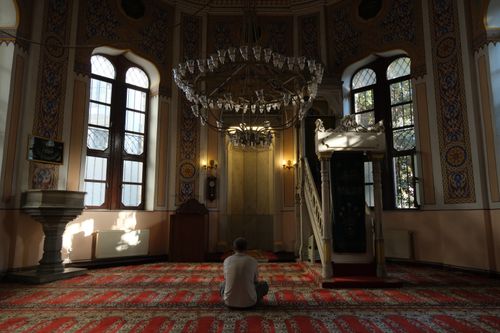 Free A man sits in prayer under a chandelier in an intricately decorated mosque. Stock Photo