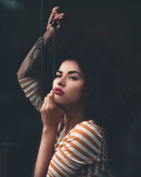 Striking portrait of a woman with afro hair and striped top against a dark background.