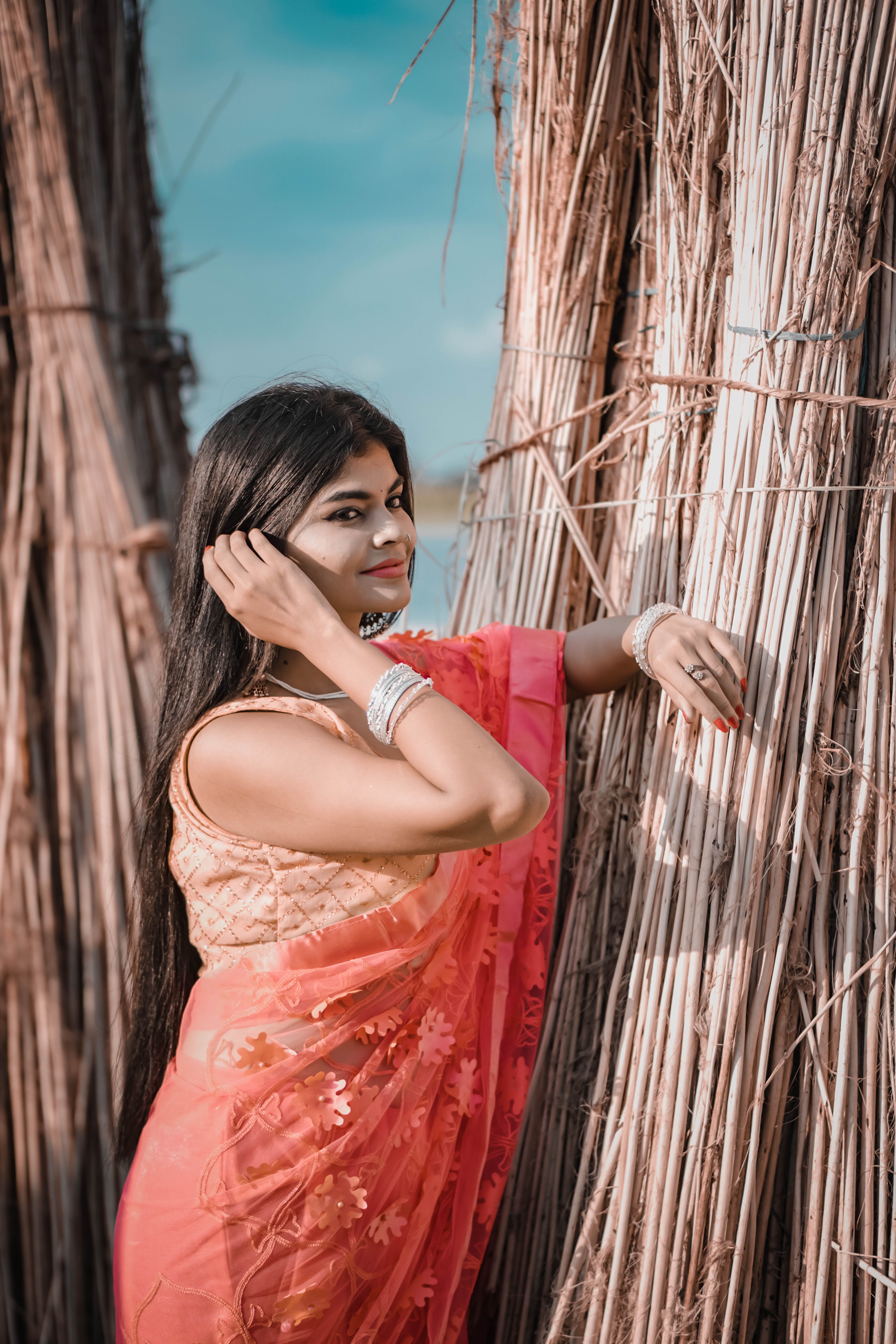 South Asian woman in a vibrant saree poses elegantly in an outdoor setting, embodying traditional beauty.