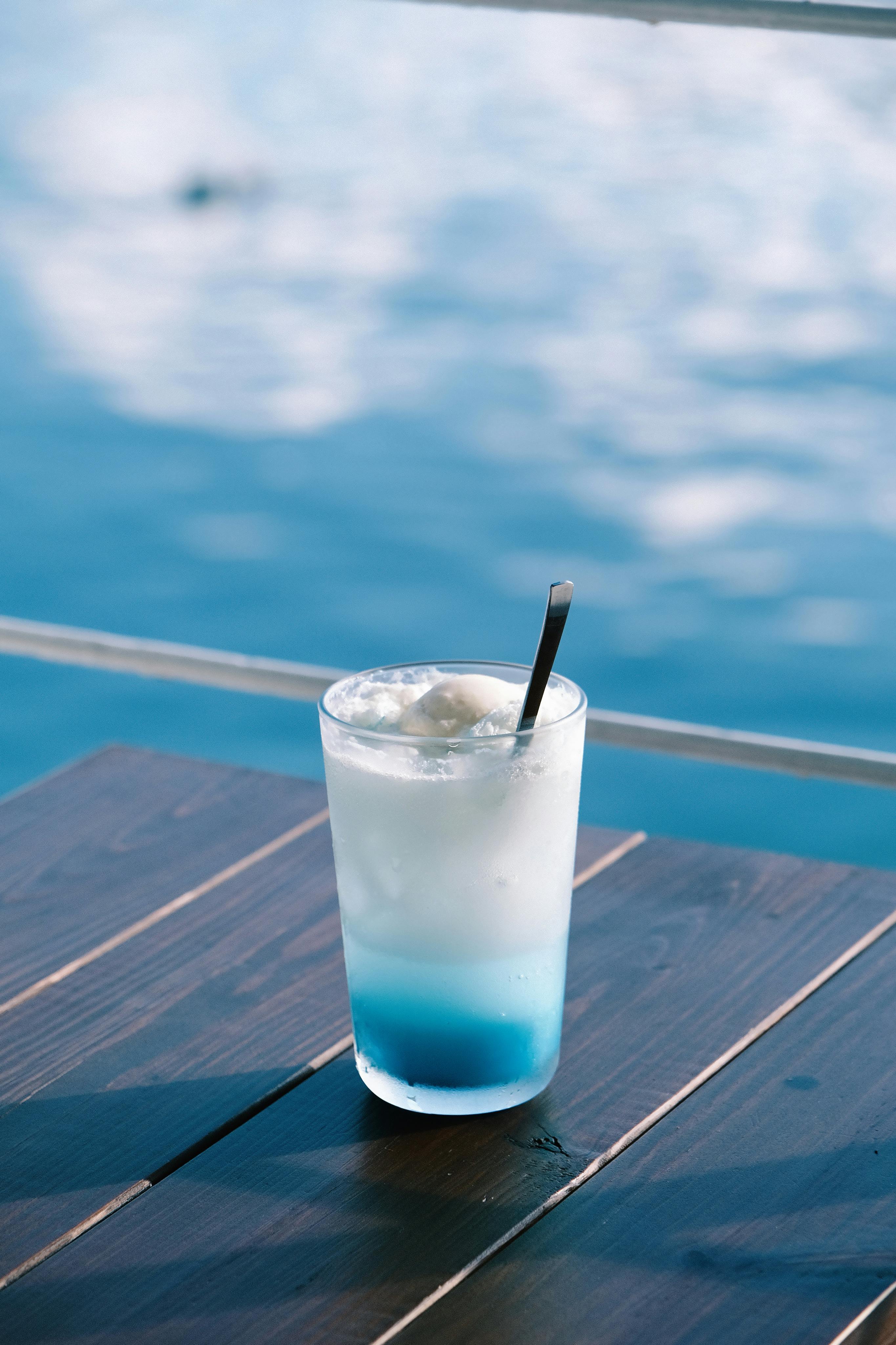Chilled blue cocktail on wooden table by the sea, perfect for summer relaxation.