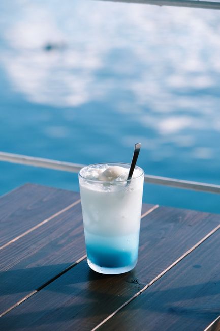 Chilled blue cocktail on wooden table by the sea, perfect for summer relaxation.