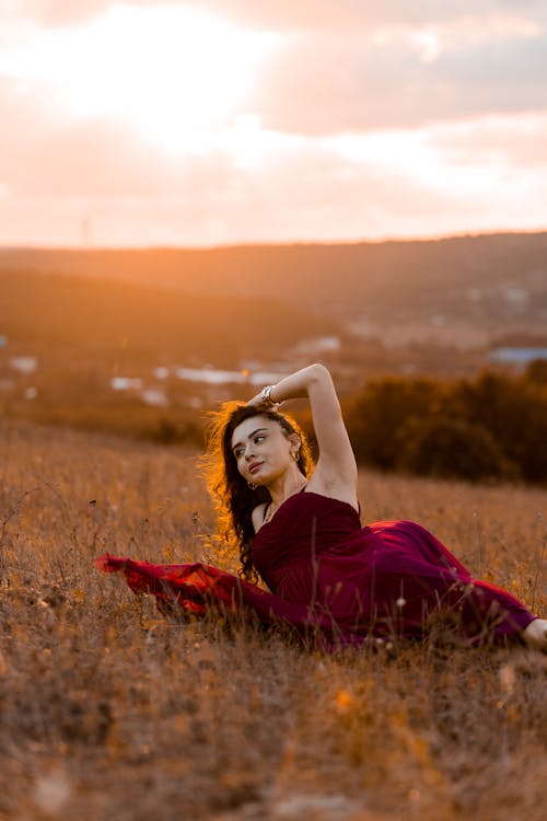 Woman in Red Dress Lying Down on Grassland at Sunset