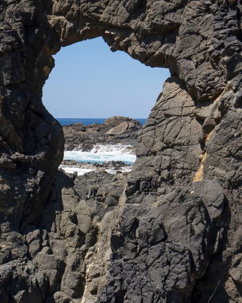 Free Striking view of ocean waves through rugged rock formations under a clear blue sky. Stock Photo