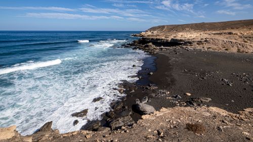 Free Breathtaking view of a rocky coastline with waves crashing against the shore under a clear blue sky. Stock Photo