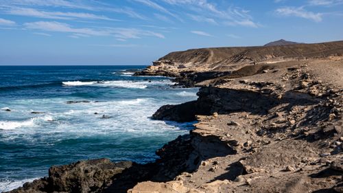 Free A stunning view of a rocky coastline with waves crashing and a clear blue sky. Stock Photo