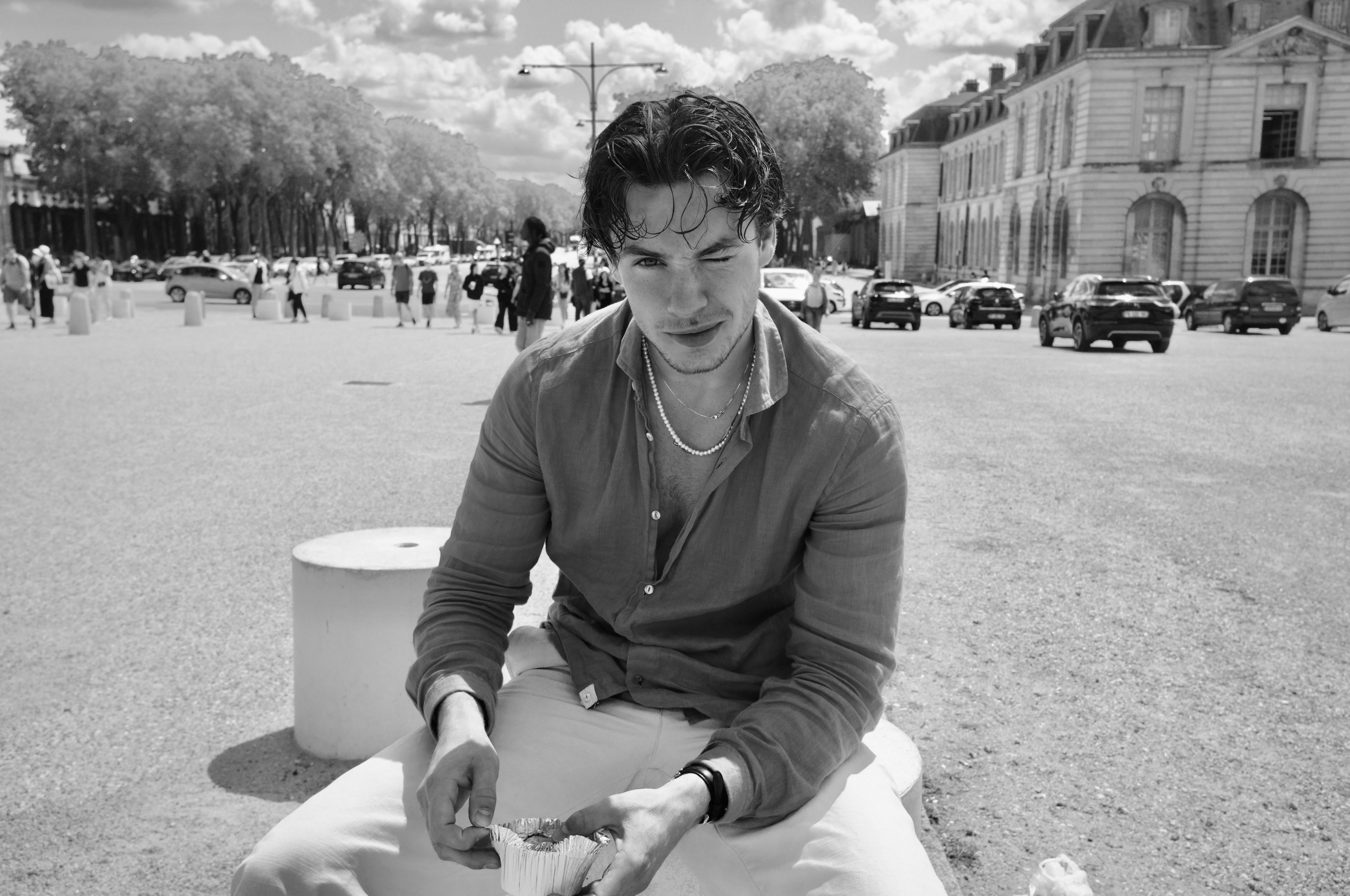 Monochrome street portrait of a young man sitting outdoors in a European city.