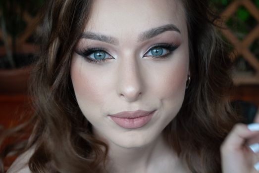 A close-up portrait of a woman with blue eyes and professional makeup, exuding elegance.
