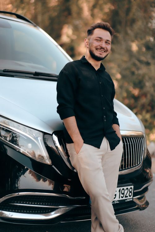 Free Casually dressed man smiling and leaning against a luxury car on a sunny day. Stock Photo