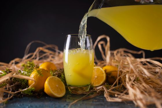 Lemonade pouring from a pitcher into a glass among lemons and dried straw