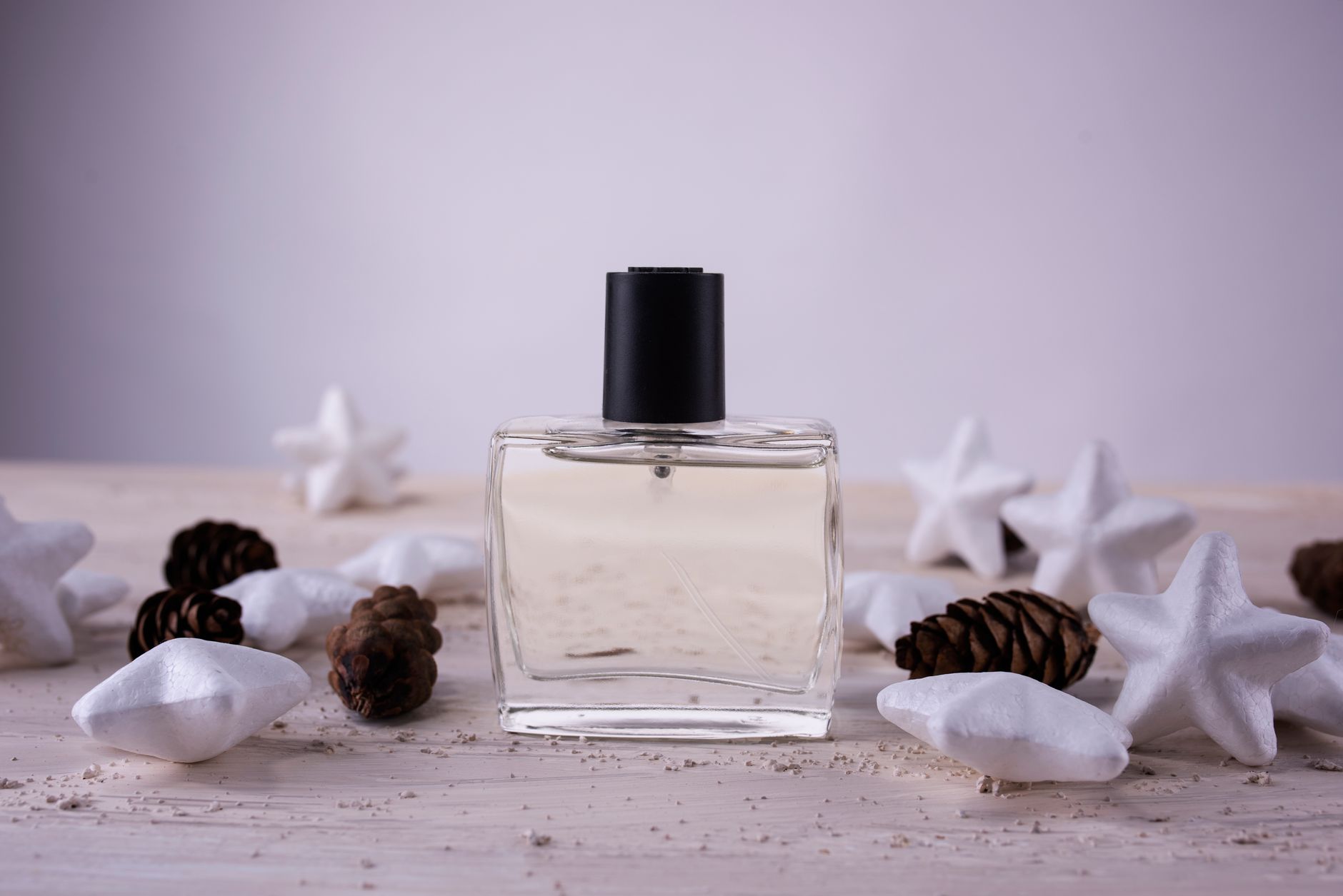 A glass perfume bottle surrounded by pine cones and white stars on a wooden surface.