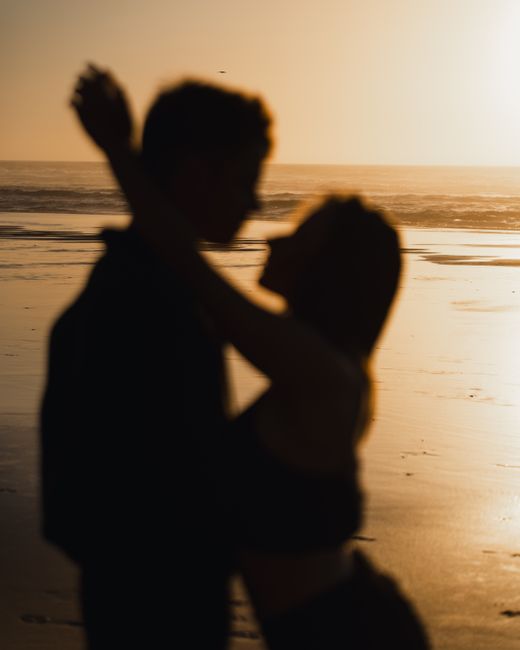 Couple embracing on a beach at sunset, creating a romantic silhouette against the ocean backdrop.