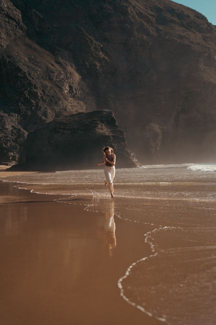 A woman running along a rocky beach with waves, reflecting the serene and calming summer atmosphere.