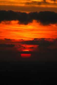 A captivating red sunset with clouds partially covering the sun, creating a dramatic and warm evening sky.