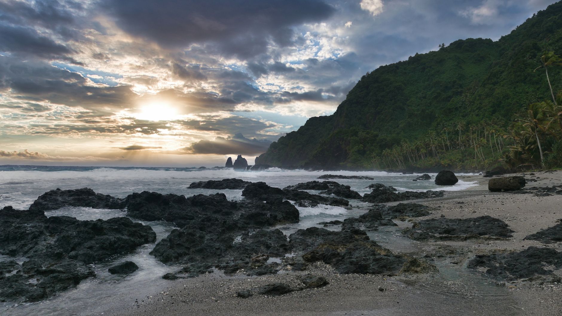 Dramatic sunset over a rocky coastline with lush hills and ocean waves, showcasing nature's beauty.