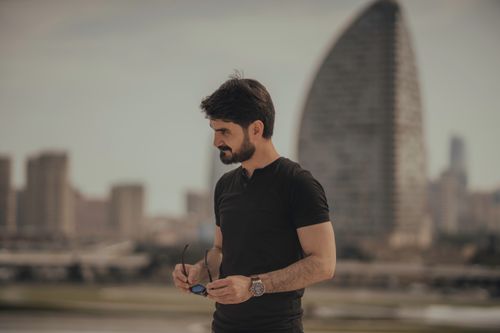 Free Stylish man in modern cityscape, holding sunglasses with a thoughtful pose. Stock Photo