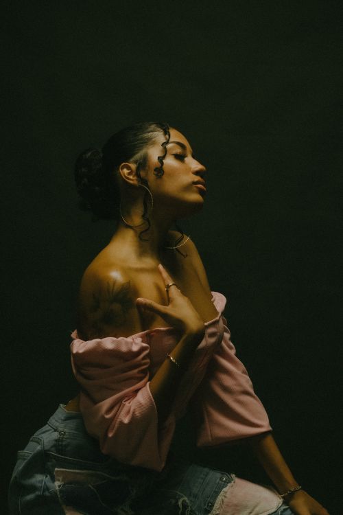 Free Graceful woman in pink attire posing in a dark, moody portrait with a black background. Stock Photo