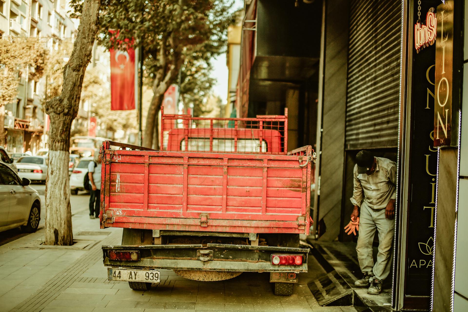 A red delivery truck parked on a city street with a worker nearby during the day.