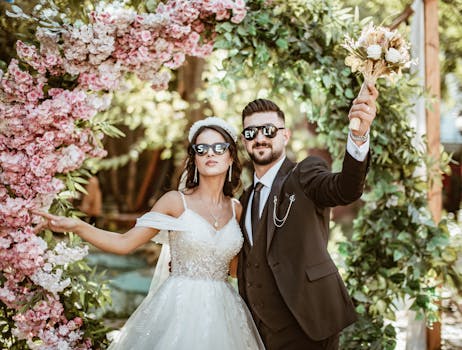 Cheerful couple posing with flowers under a floral arch at their wedding.