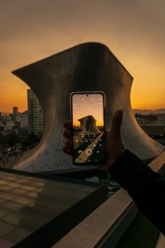 A person capturing the iconic Soumaya Museum at sunset, showcasing modern architecture and vibrant cityscape.