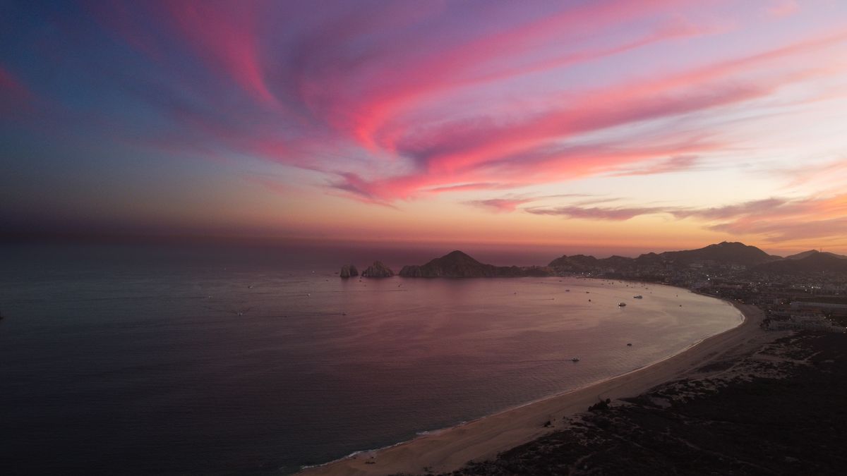 A breathtaking aerial shot of Cabo San Lucas at sunset, showcasing vibrant pink 