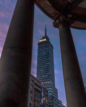 View of Torre Latinoamericana skyscraper framed by columns during dawn in Mexico City.