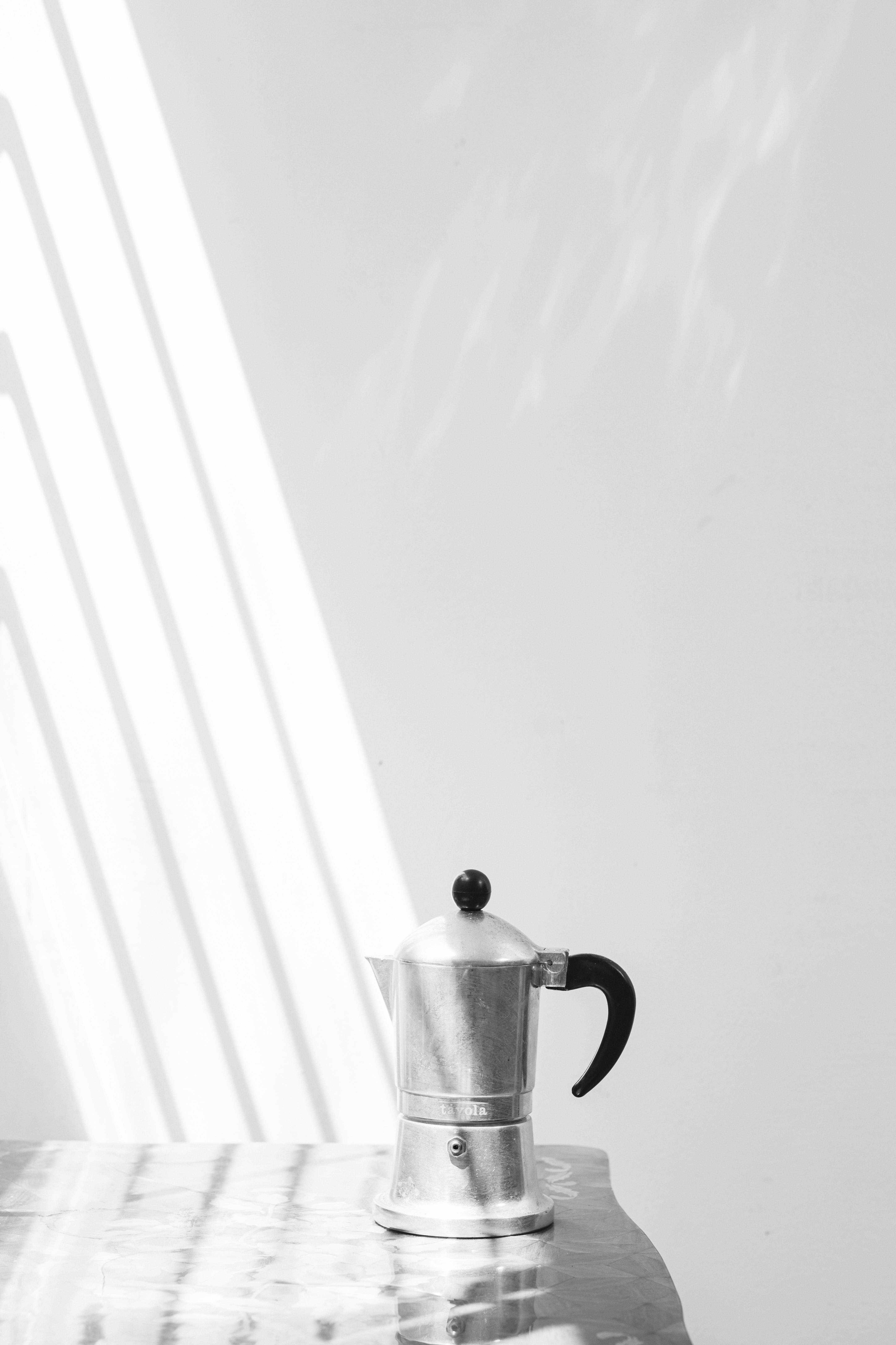 Elegant minimalist black and white photo of a stainless steel moka pot casting shadows.