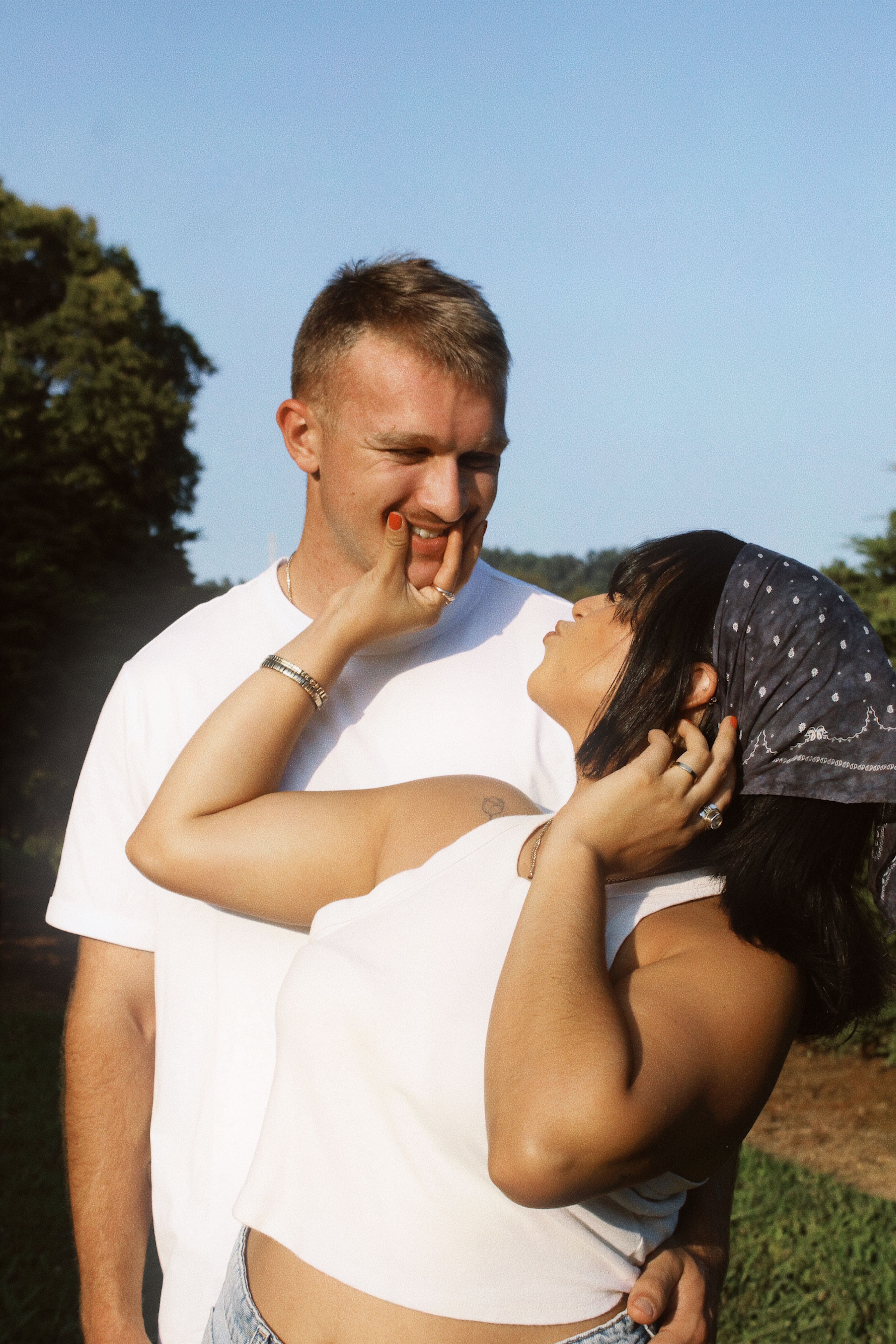 Affectionate couple smiling at each other in a sunny outdoor setting, embracing love and happiness.