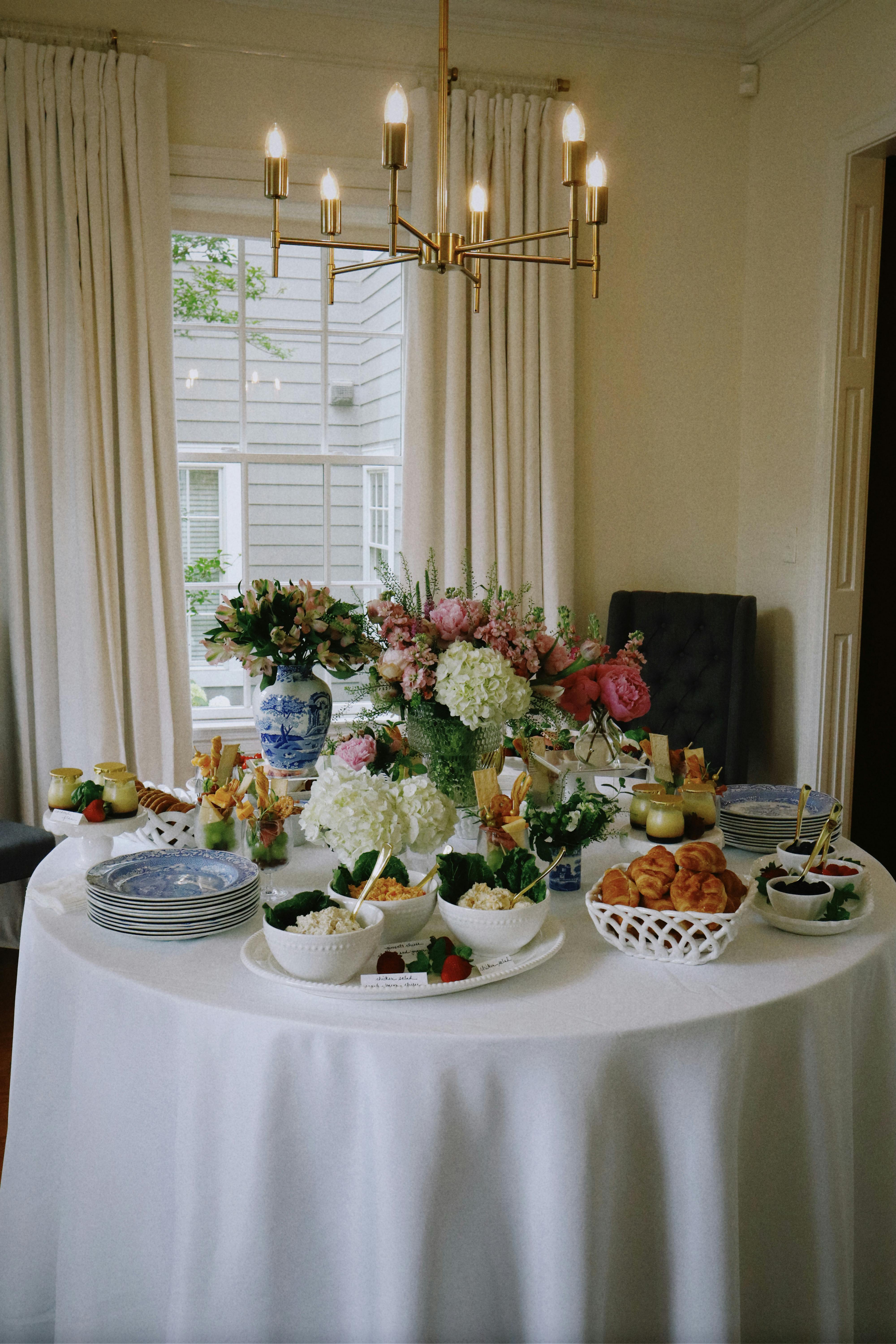 A beautifully arranged table with flowers, food, and an elegant chandelier above, perfect for a sophisticated gathering.