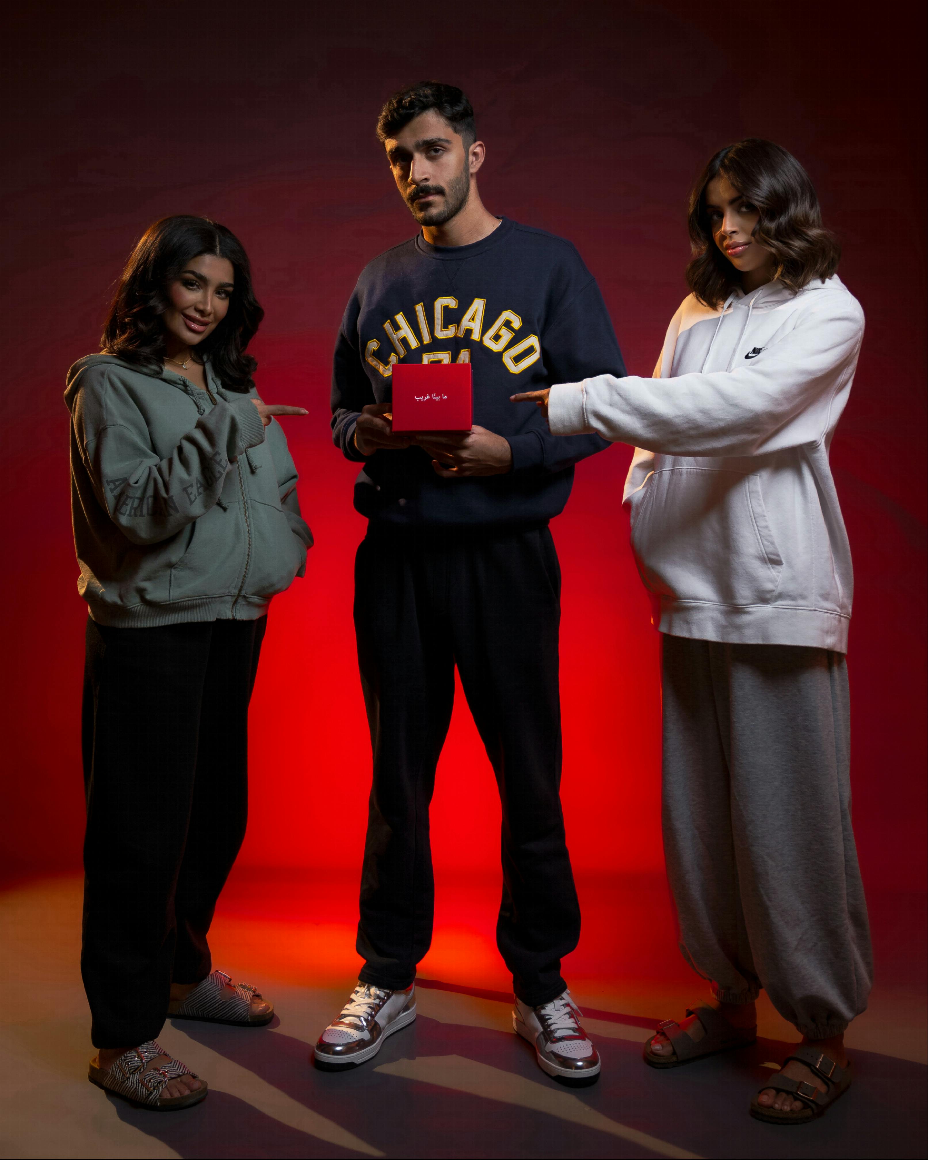 Three adults in stylish hoodies pose in a studio with a dramatic red backdrop.