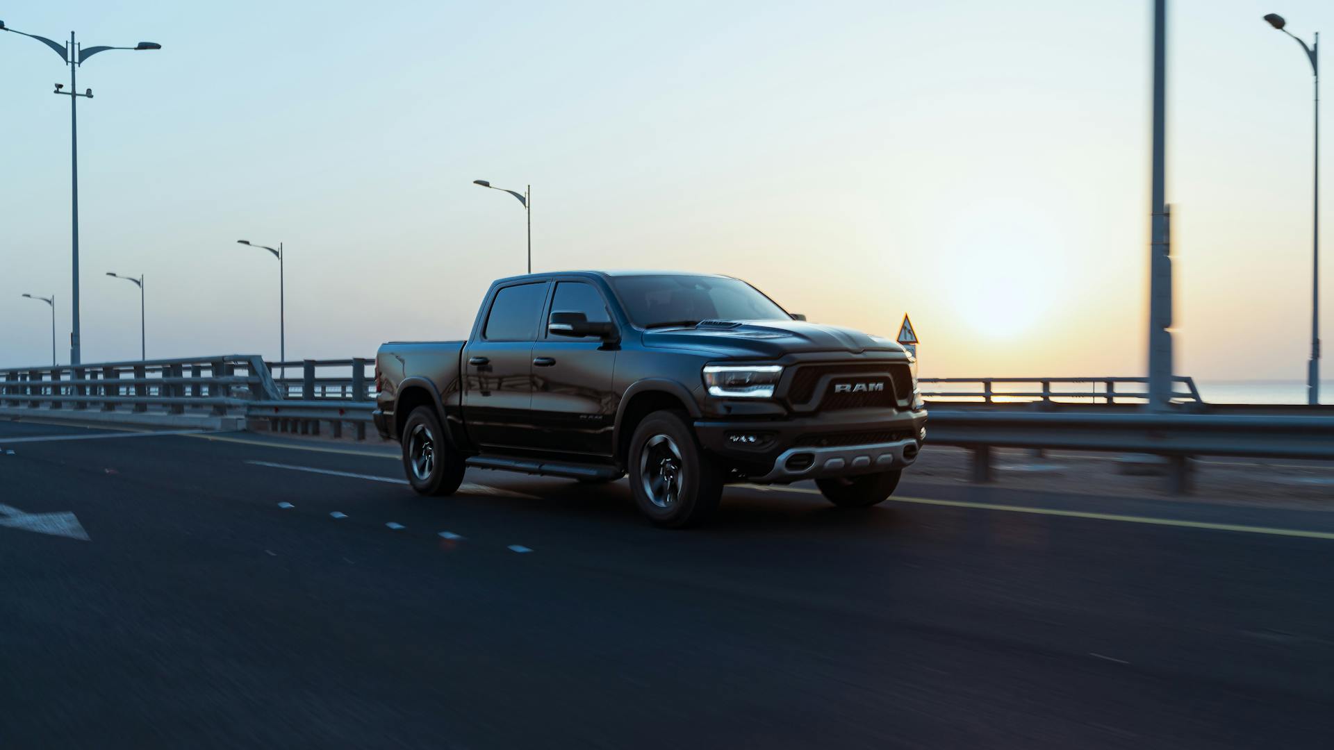 A sleek black Ram pickup truck speeds down an empty highway at sunrise, showcasing modern design and power.