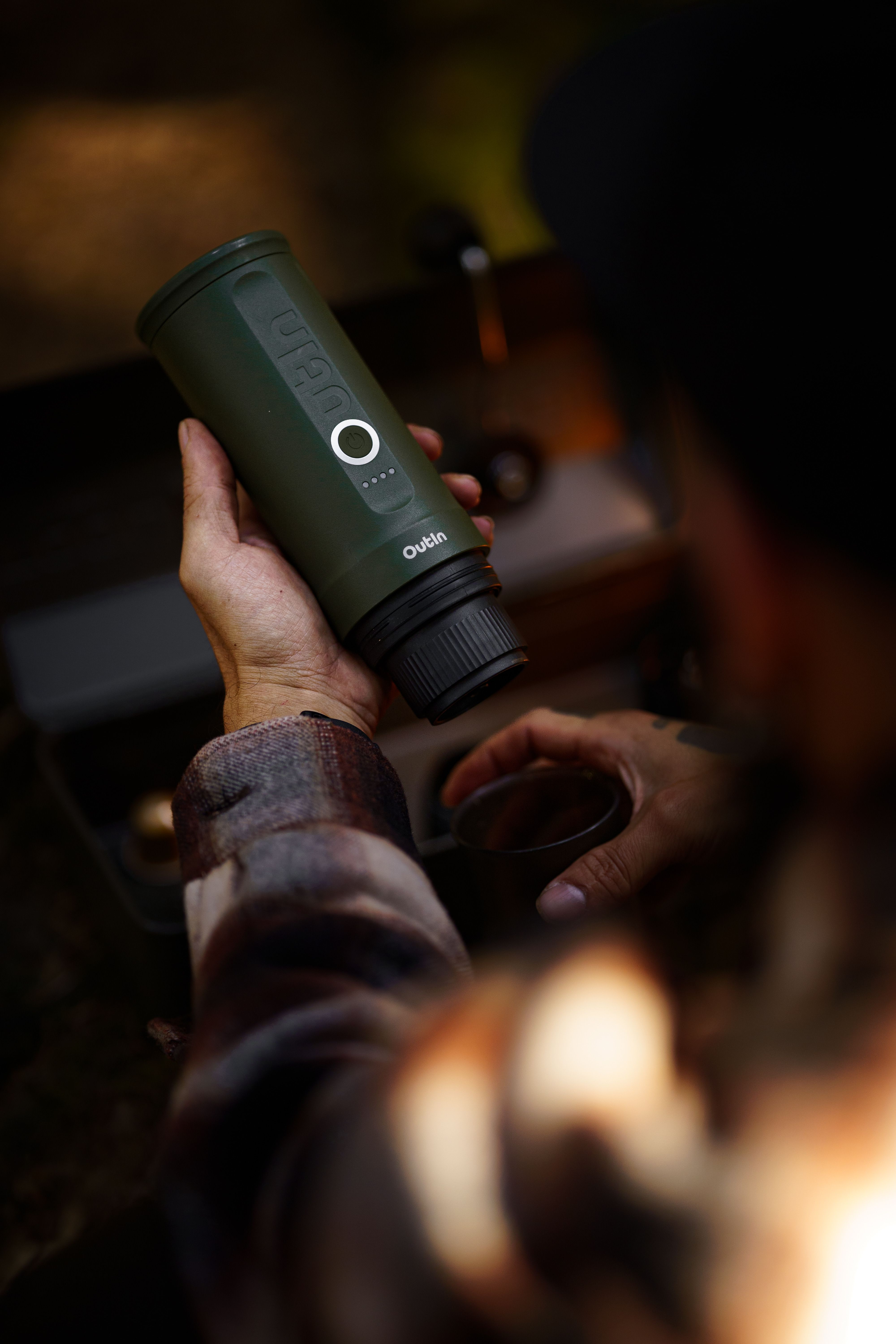 Travel cup clamp holding an insulated mug on a camp chair armrest at a campsite