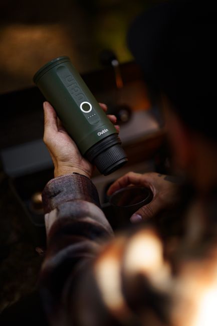 Travel cup clamp holding an insulated mug on a camp chair armrest at a campsite