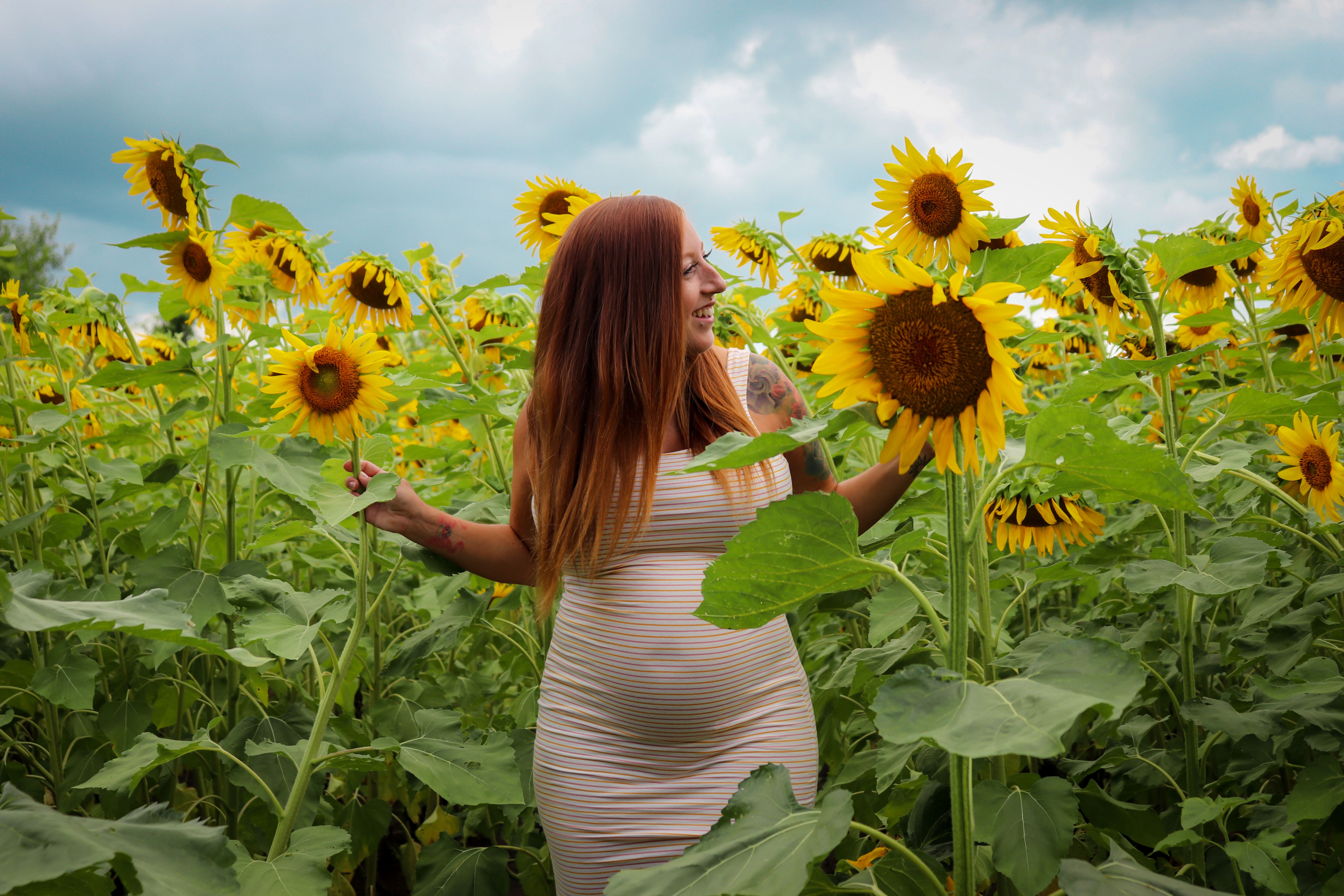 Pregnant woman smiling among vibrant sunflowers on a sunny day, embodying positivity.