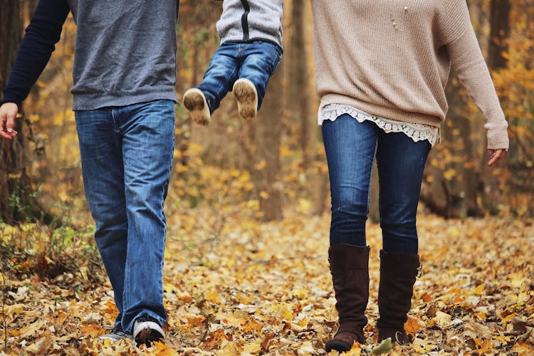 Legs Of A Couple Walking In Autumn Forest With A Child