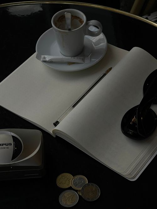 Free A calming café scene with a coffee cup, open notepad, coins, and sunglasses on a table. Stock Photo