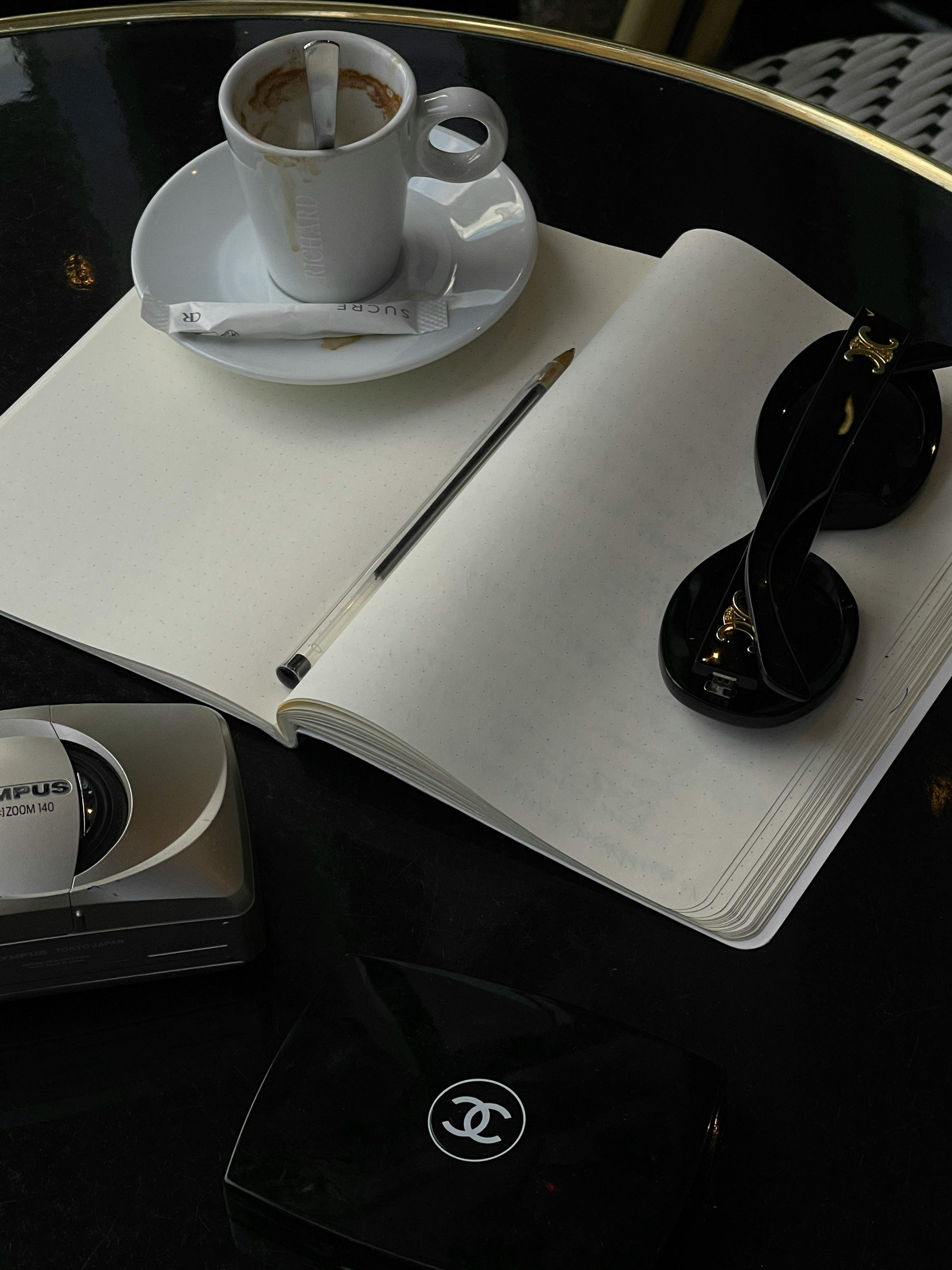 Elegant setup with coffee, notebook, and sunglasses on a café table.
