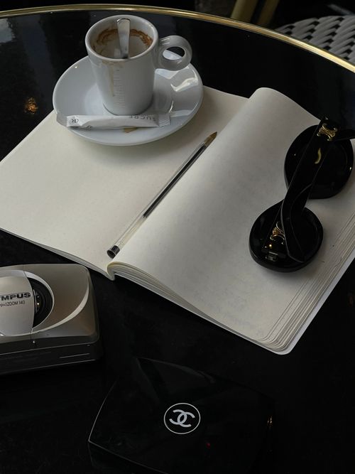 Free Chic café scene with coffee, notebook, pen, and sunglasses on a table. Stock Photo