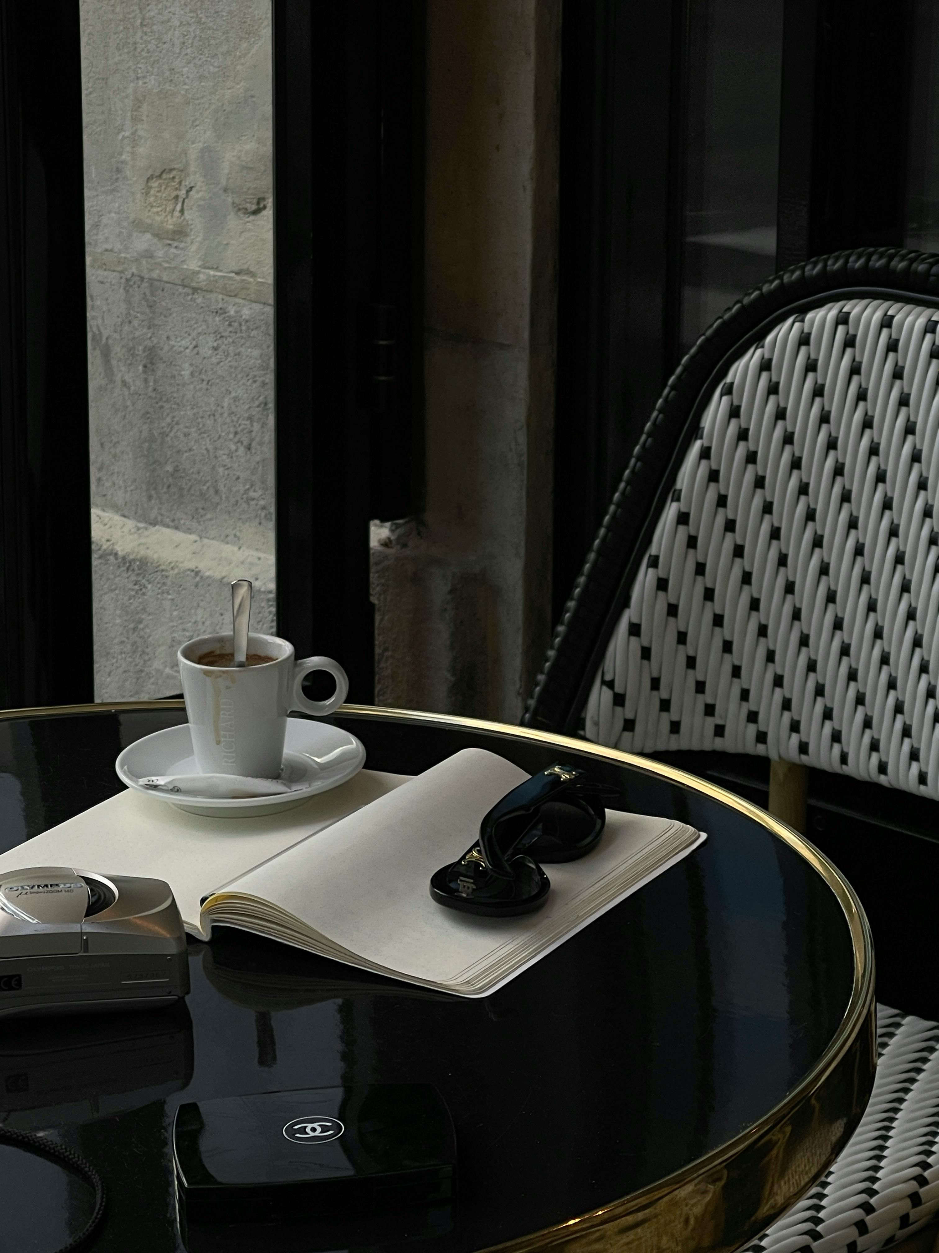 Elegant café scene with espresso, notepad, and sunglasses on a stylish table.