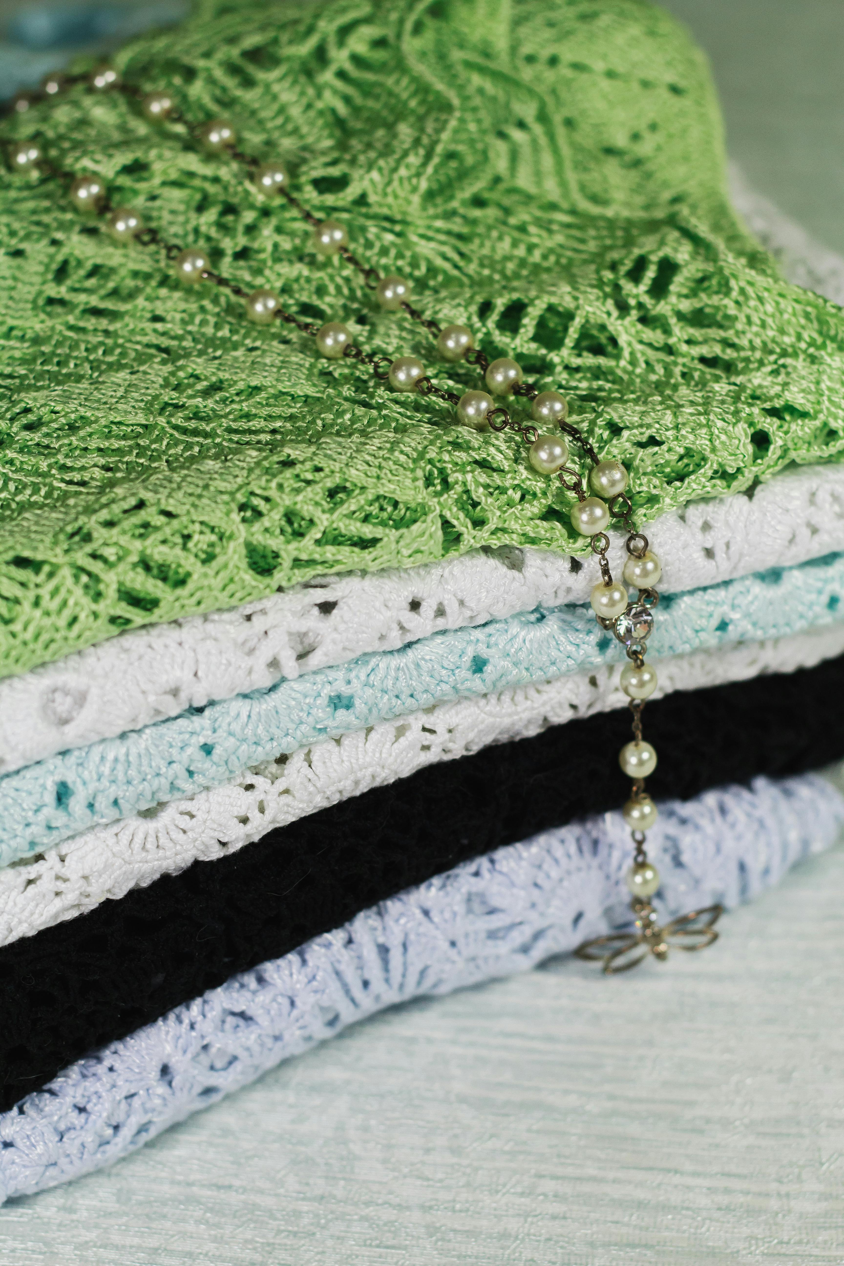 Close-up of stacked colorful knitted fabrics with a pearl necklace draped on top, showcasing texture and elegance.