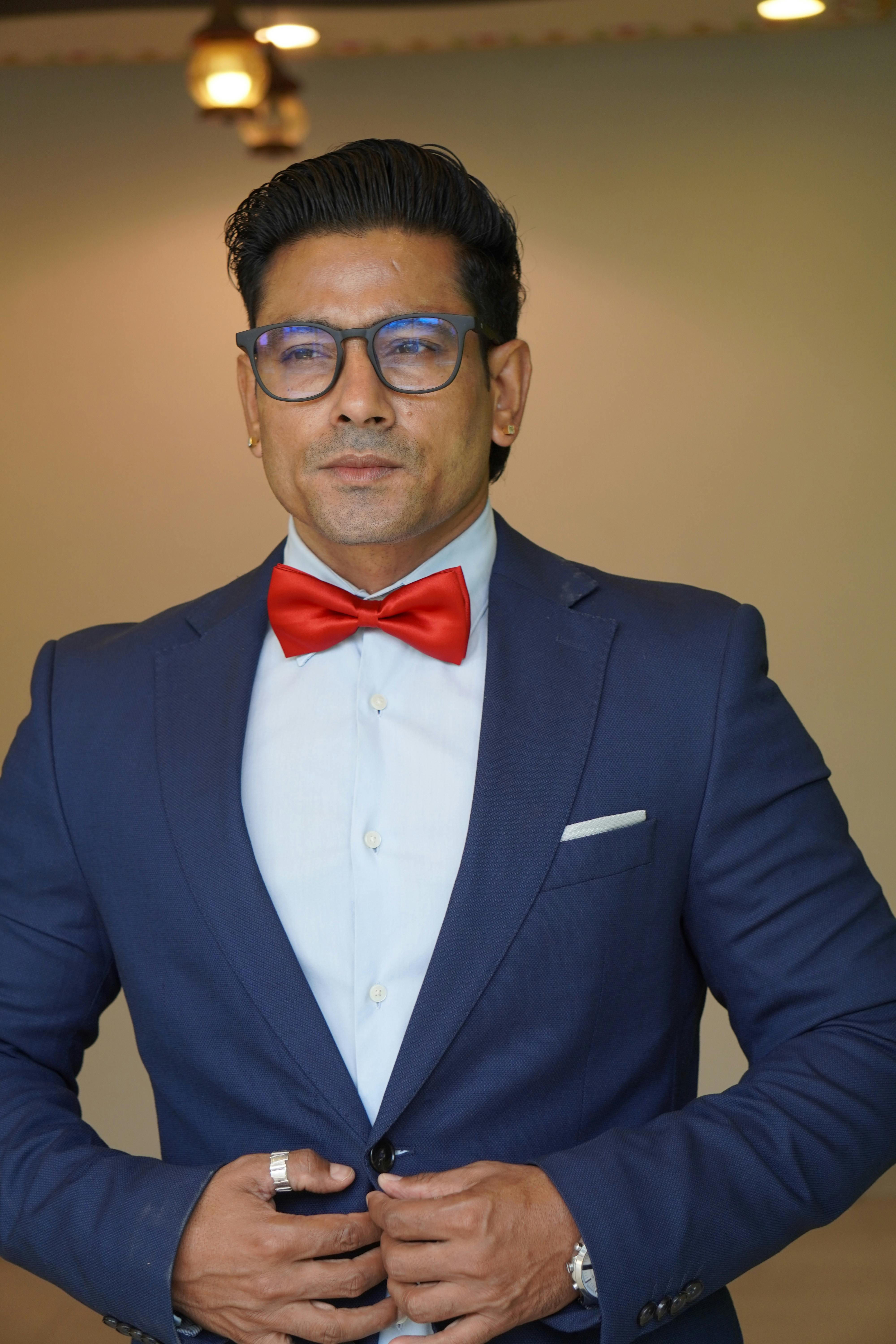 Elegant portrait of a man in a formal suit, red bow tie, and eyeglasses indoors.