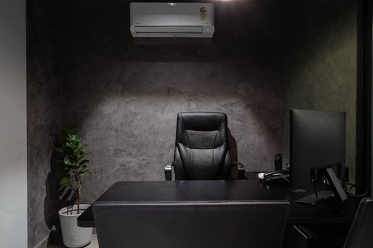Minimalist office interior featuring leather chair, desk, monitor, plant, and air conditioner.