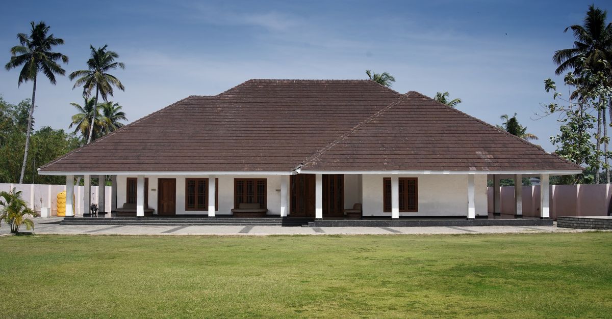 A traditional tropical bungalow surrounded by palm trees and lush green lawn.