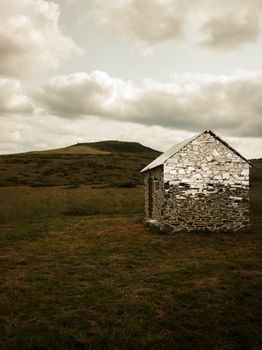 Mirror-covered house in a grassy field under cloudy skies, blending art with nature.