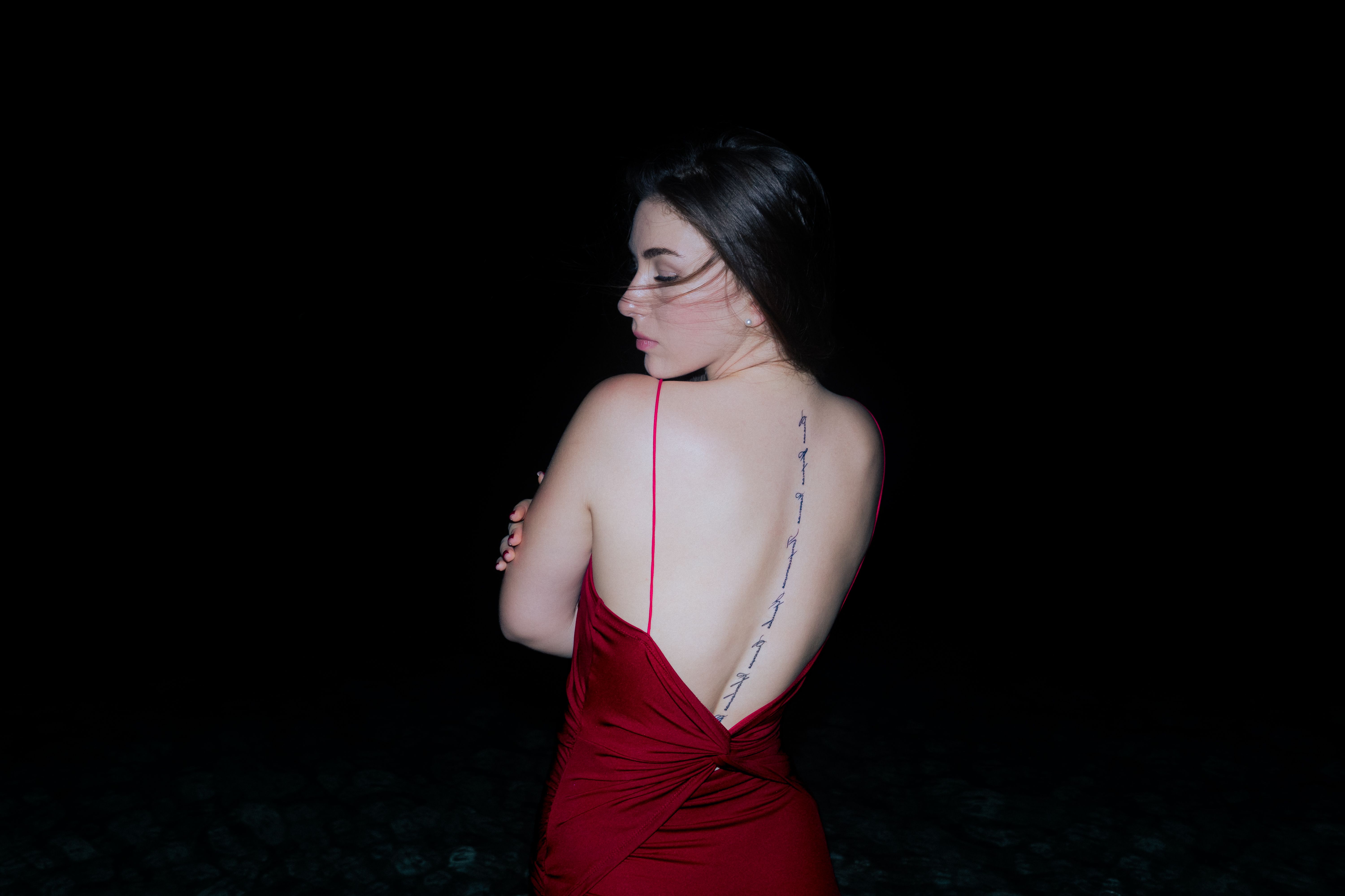A stylish woman in a red dress poses with a black background, highlighting elegance and fashion.