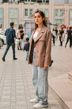 Stylish young woman poses outdoors in city environment, showcasing fashion trend.