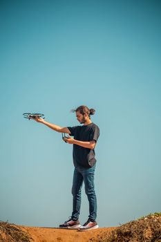 Young man using a drone on a sunny day with a clear sky backdrop.