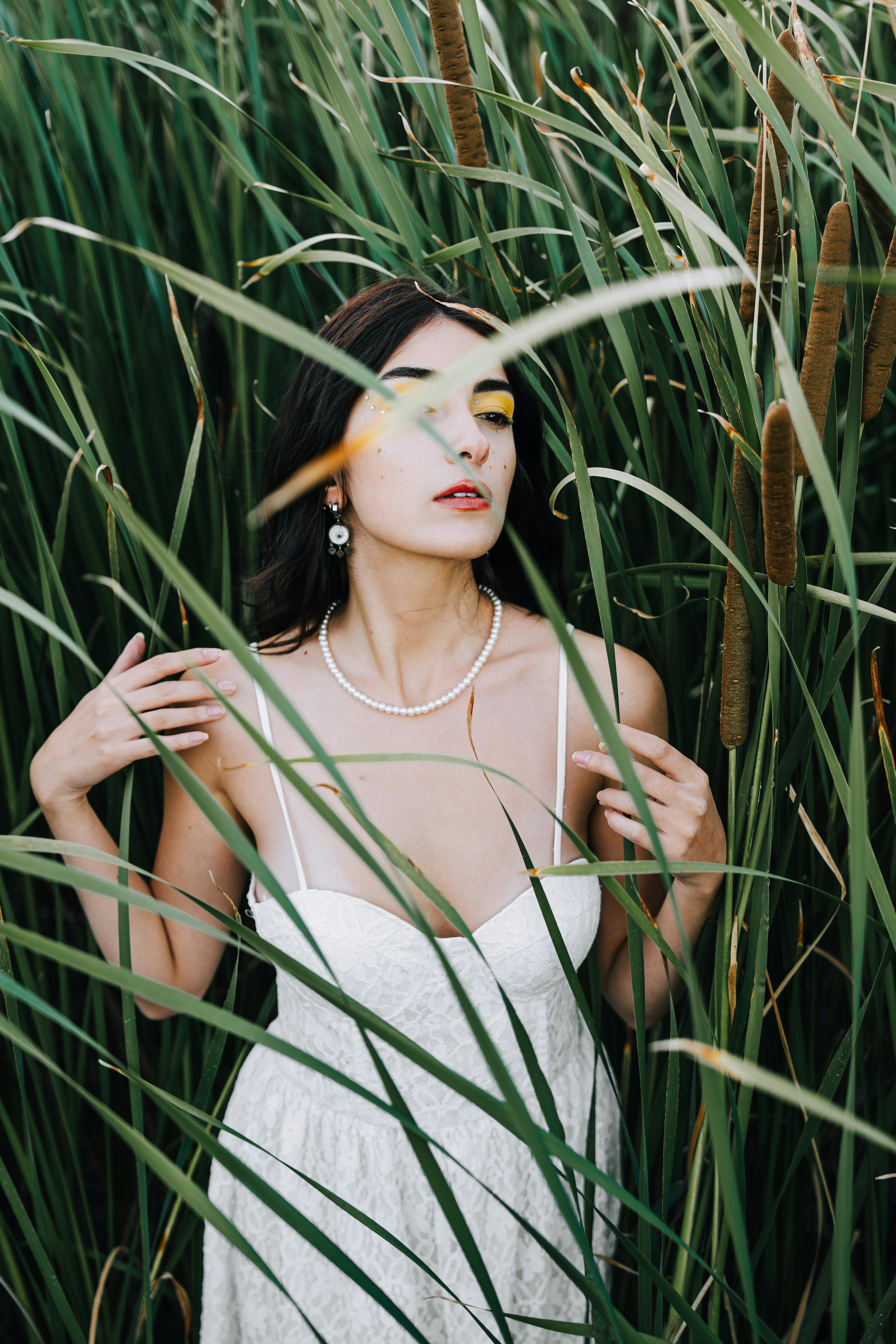 A woman in a white dress stands gracefully among tall grass, exuding natural elegance and beauty.