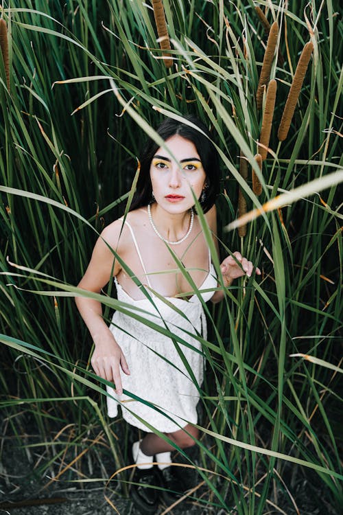 Model in White Summer Dress Standing in Tall Grass and Looking Up