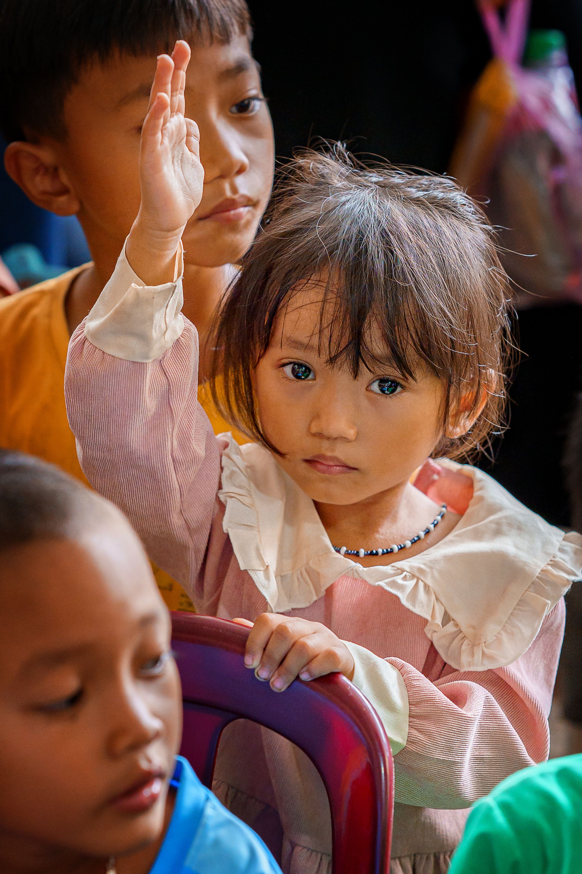 A girl raising her hand amid classmates, displaying participation
